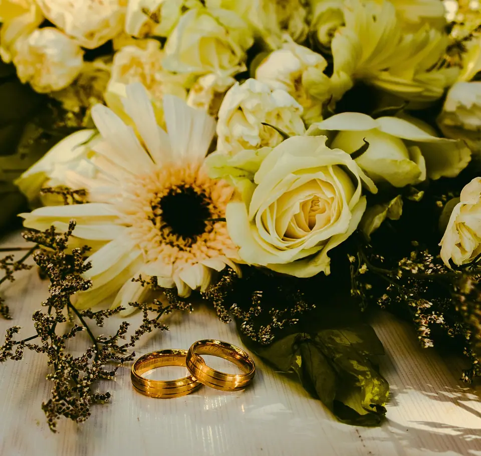 Gold rings beside a white rose bouquet