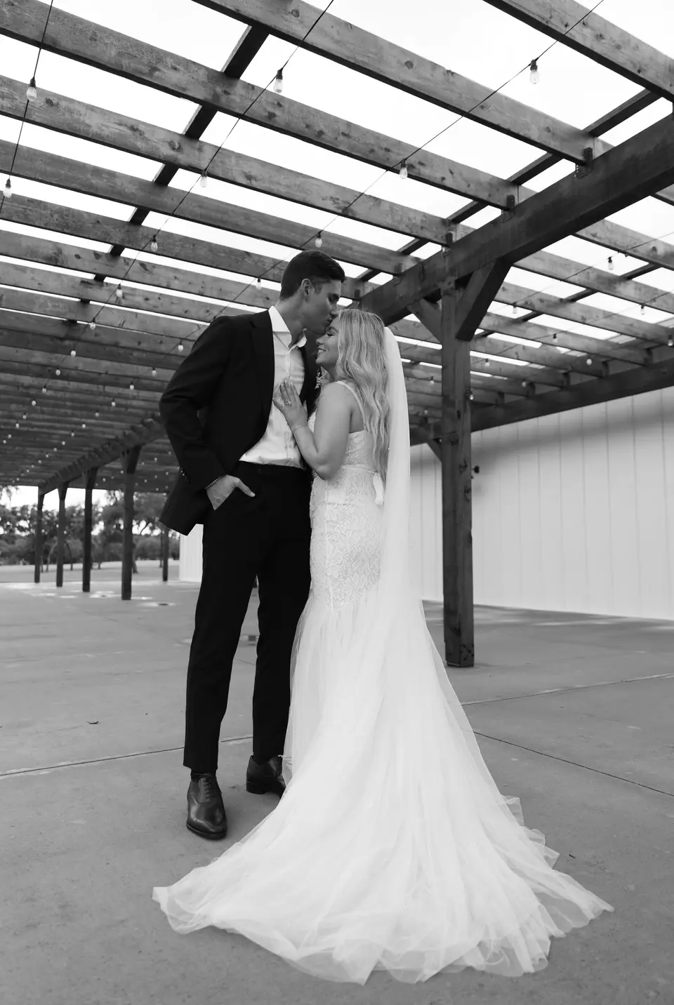 Newlyweds kissing under a pergola, black and white