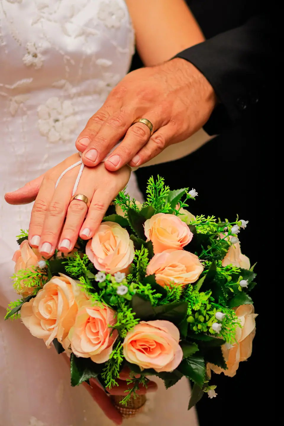 Hands with wedding rings over a peach bouquet